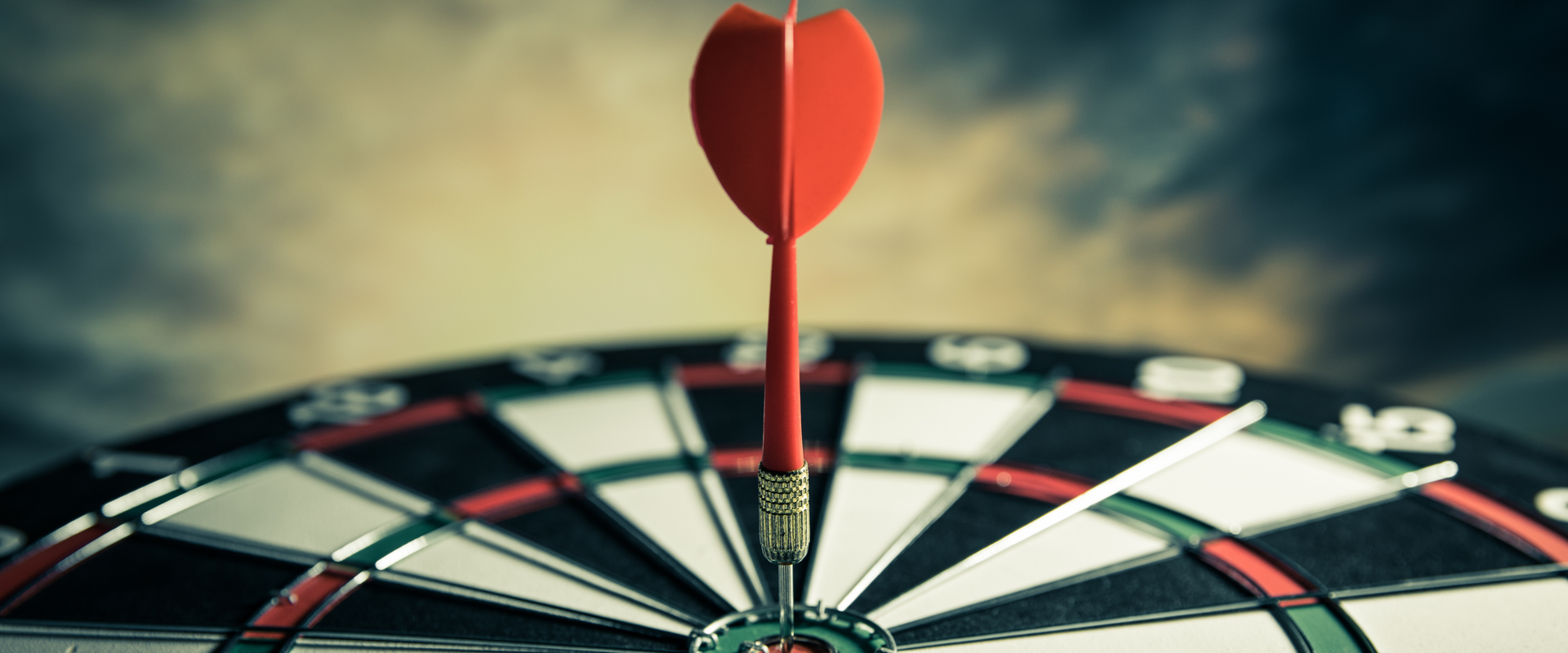 Red dart hitting the bullseye of a dartboard against a dramatic sky